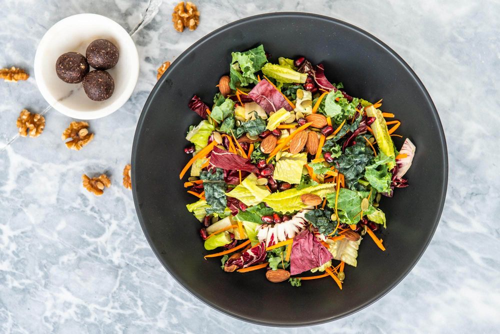 Colorful salad with vegetables and nuts served in dark bowls on a light surface.