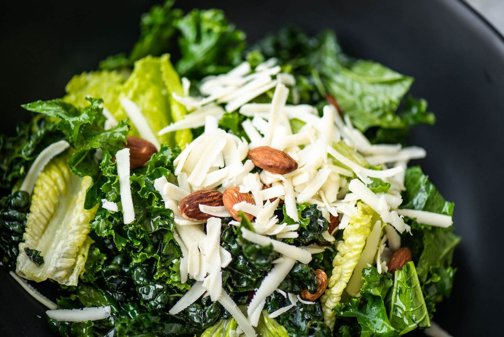 Fresh green salad with shredded cheese and lettuce in a black bowl.