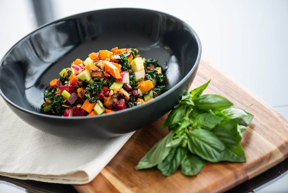Healthy grain bowls with roasted vegetables and herbs arranged on white surface.