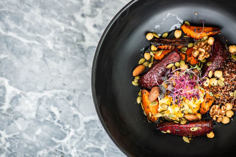 Roasted root vegetables and nuts arranged artfully on black plates with microgreens.