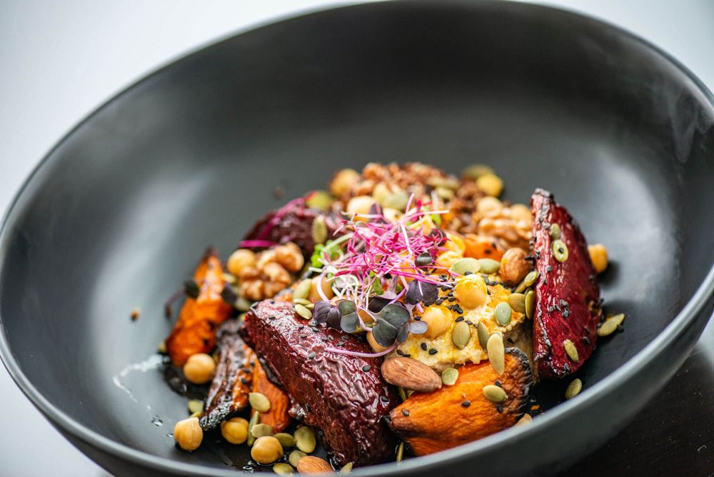 Artfully plated roasted vegetables with nuts and microgreens on black ceramic dishes.