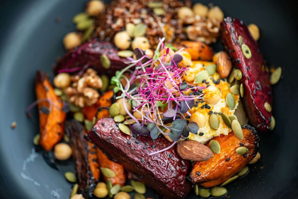 Roasted beets and carrots with nuts and microgreens plated elegantly on dark dishes.