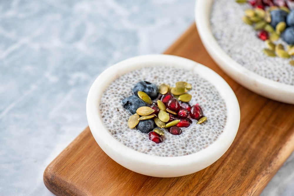 Close-up of chia seed pudding garnished with nuts, seeds and dried fruits on wooden board.