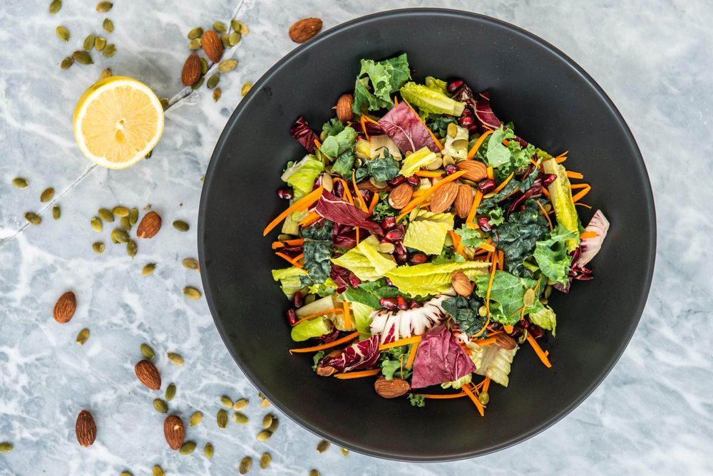 Vibrant salad bowls with colorful vegetables, nuts and citrus arranged in a row on marble surface.
