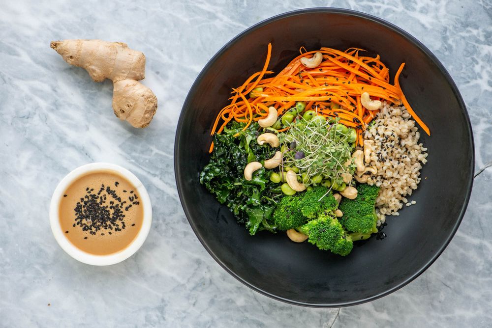 Colorful salad ingredients arranged on a black plate with quinoa, carrots, and leafy greens.