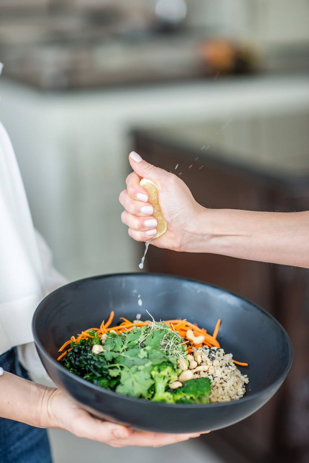 Hands holding black plates with healthy salad bowls featuring fresh vegetables and grains.