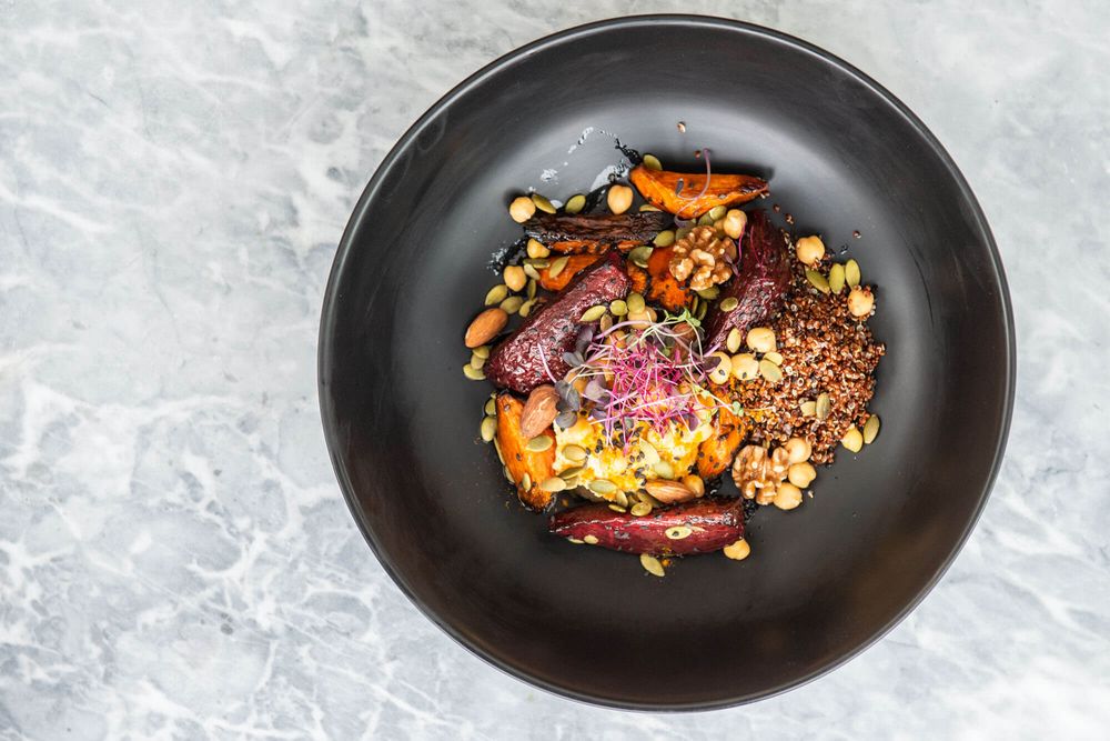 Gourmet plated dishes on black ceramic plates against marble surface.
