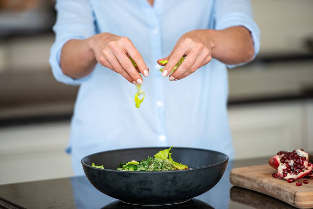 Hands preparing fresh vegetables and ingredients for healthy salad in kitchen.