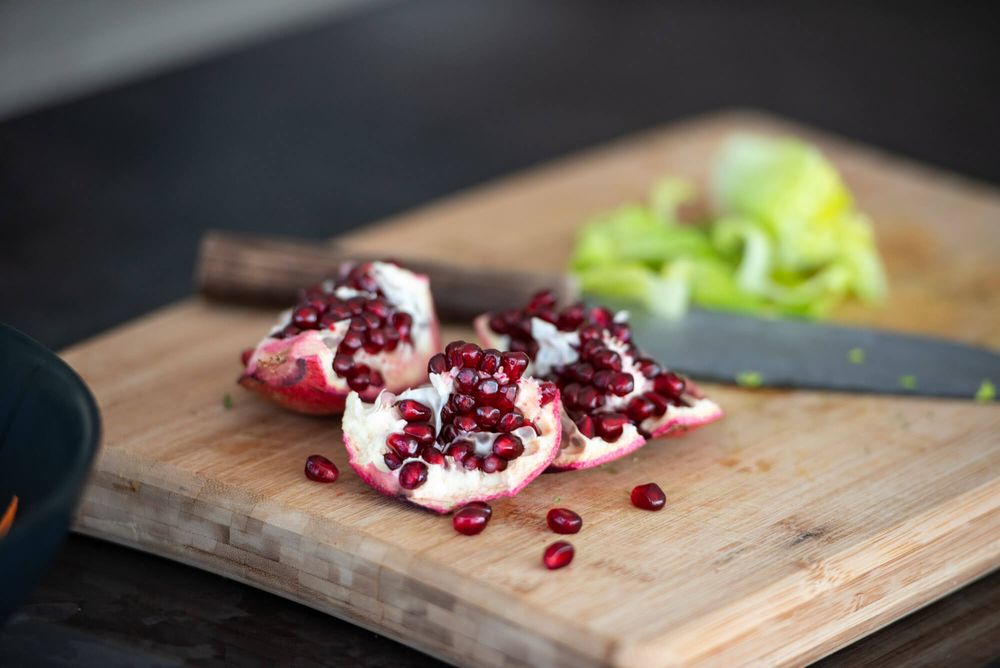 Pomegranate being deseeded on wooden cutting board with scattered arils.
