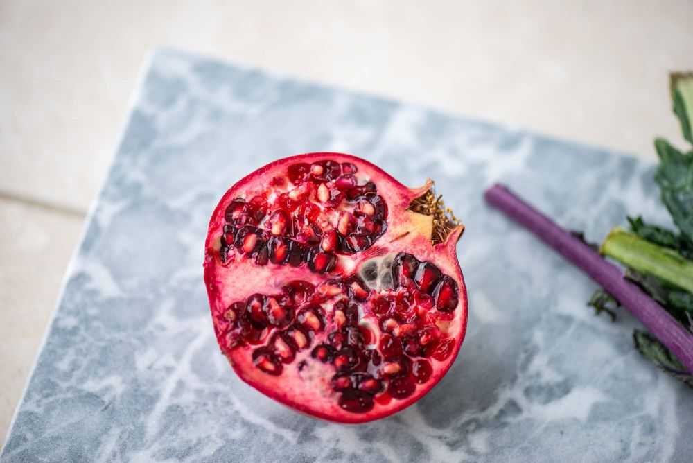 Fresh pomegranate seeds and fruit arranged on light marble surface.