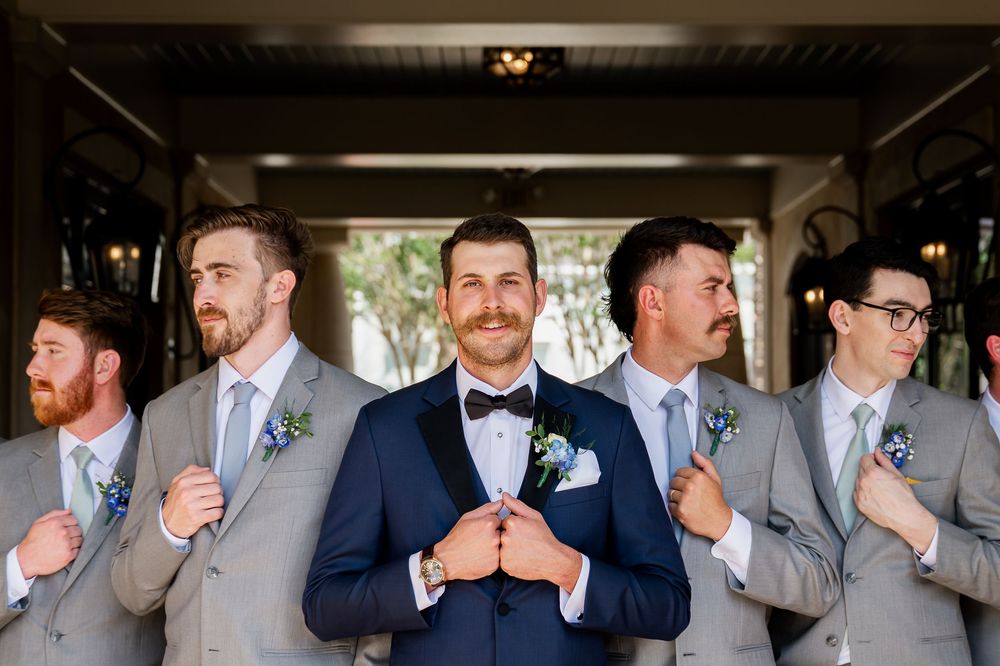 Groomsmen in navy and grey suits pose together during wedding celebrations.