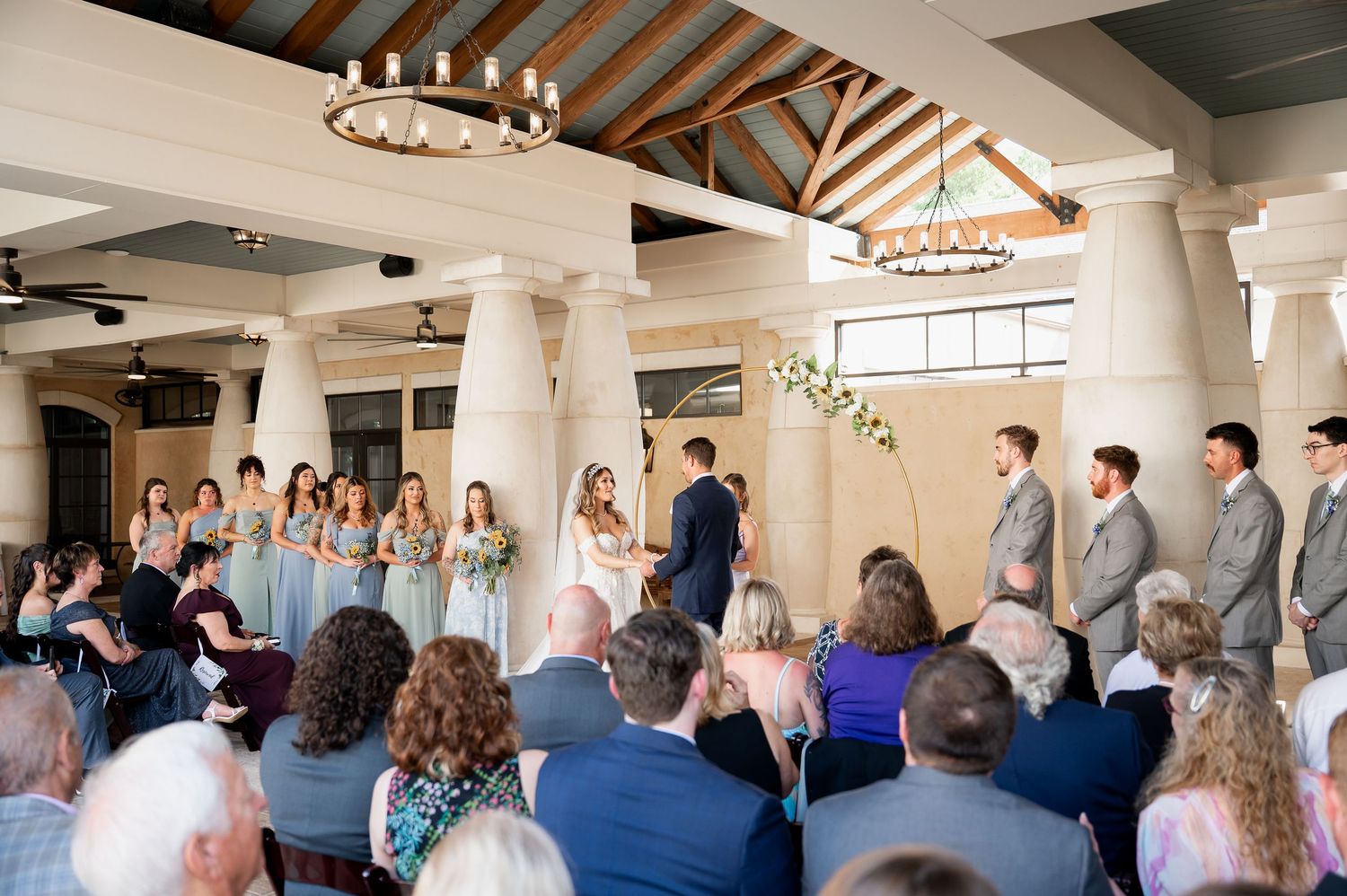 Wedding guests seated in elegant venue with exposed wooden beams and white columns.