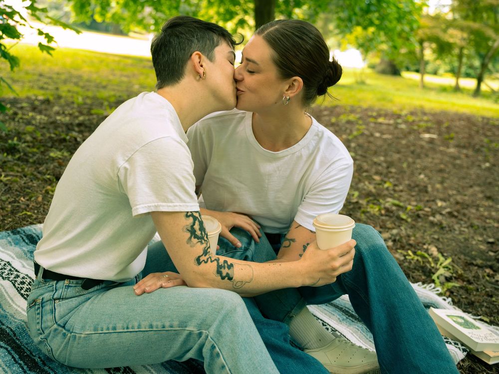 A romantic moment shared between two people in casual attire sitting on grass in a sunlit park setting.