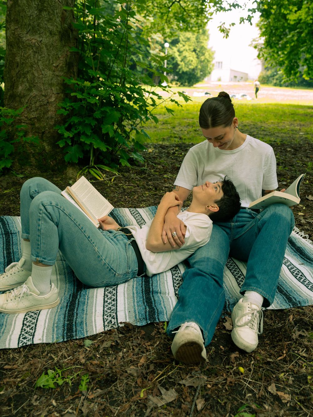A couple lying together on a striped blanket under green trees.
