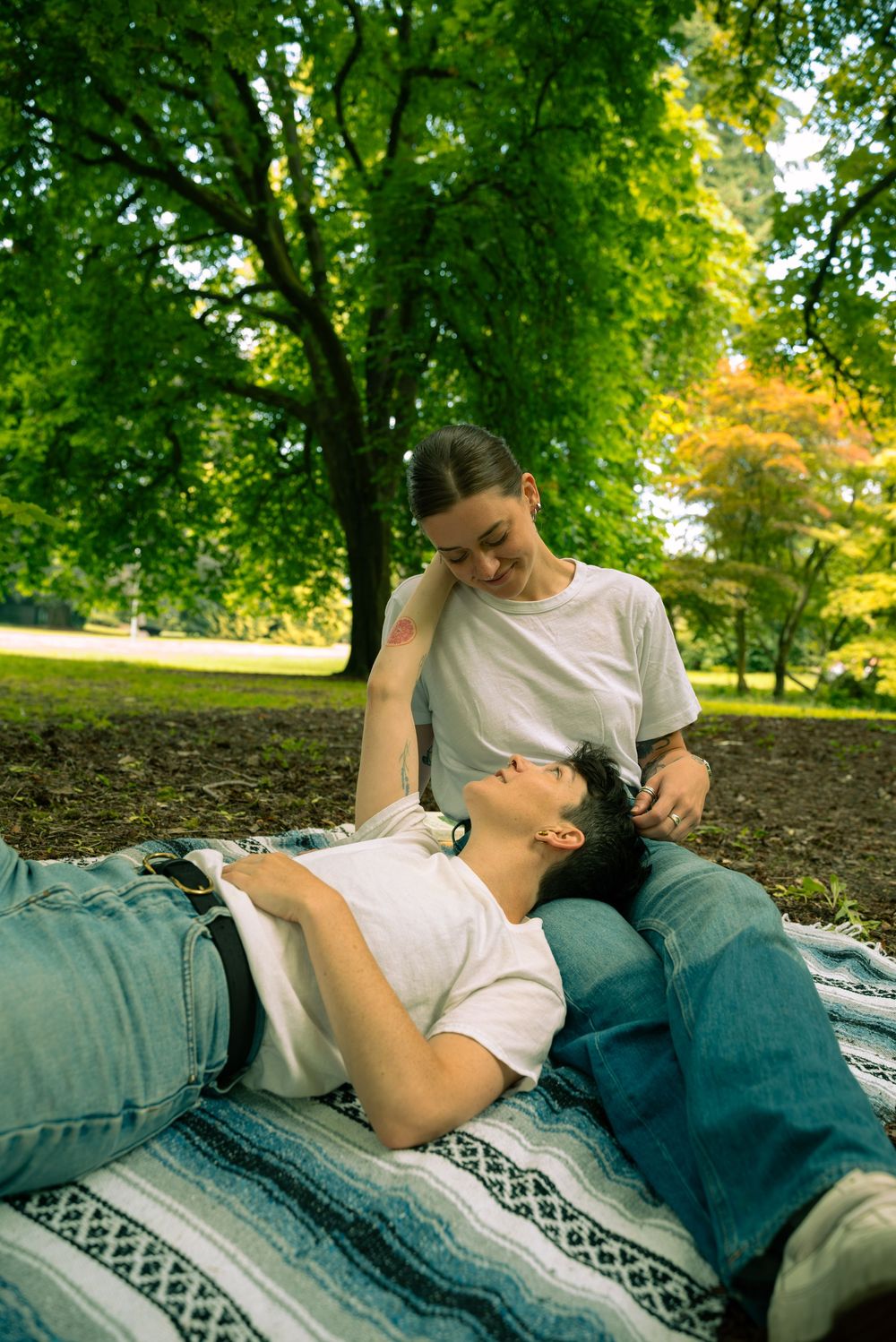 Two people sharing an intimate moment while resting on a blanket outdoors.