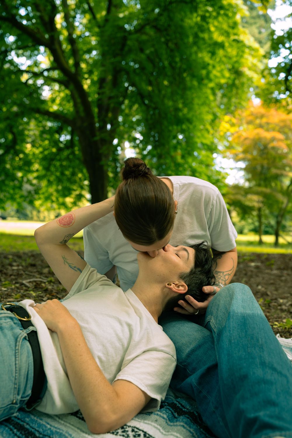 Candid moments of affection shared between two people lying on grass under green trees.