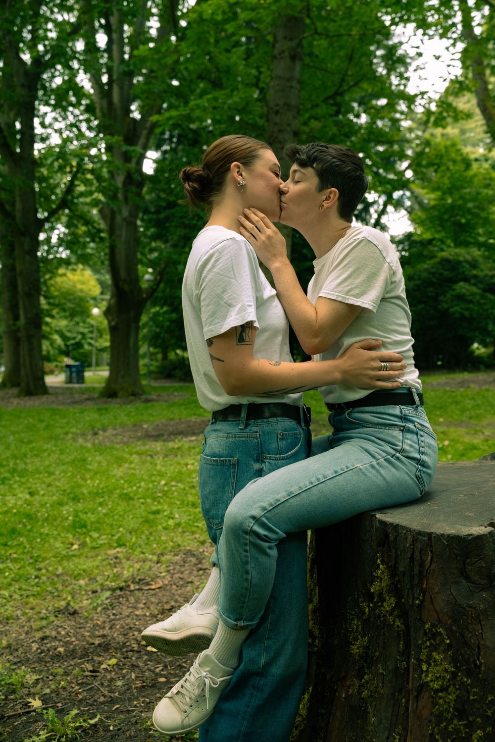 A romantic moment shared between two people sitting on a tree stump in a park.
