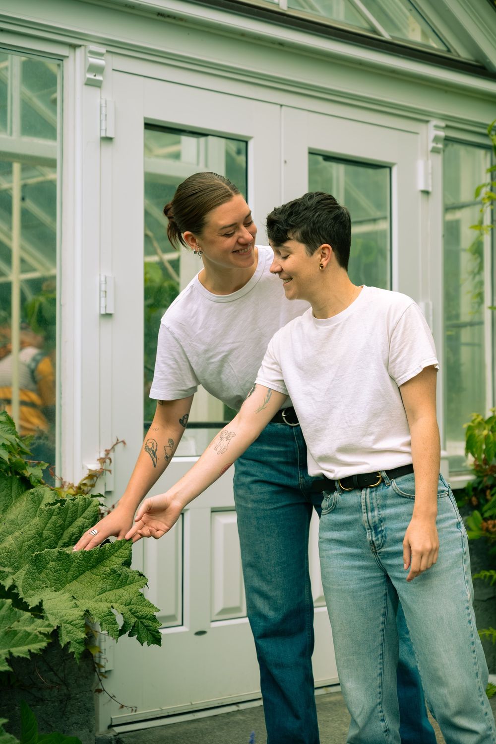 A tender moment between two people near a greenhouse with plants.