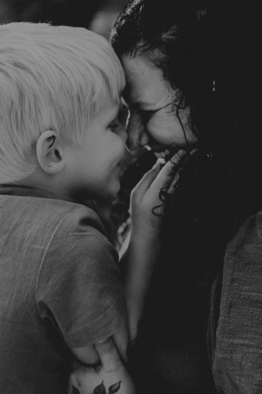 A tender black and white photograph capturing an intimate moment of affection and laughter between parent and child.