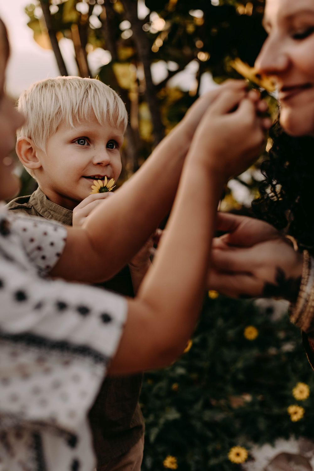 A child with light hair is being lifted up in a garden with yellow flowers in the background.