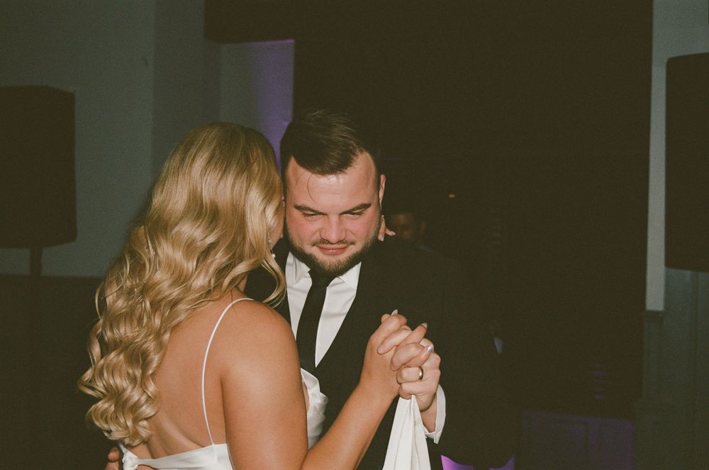 A couple shares an intimate dance moment at a wedding reception, with the bride wearing a white dress and groom in a dark suit.