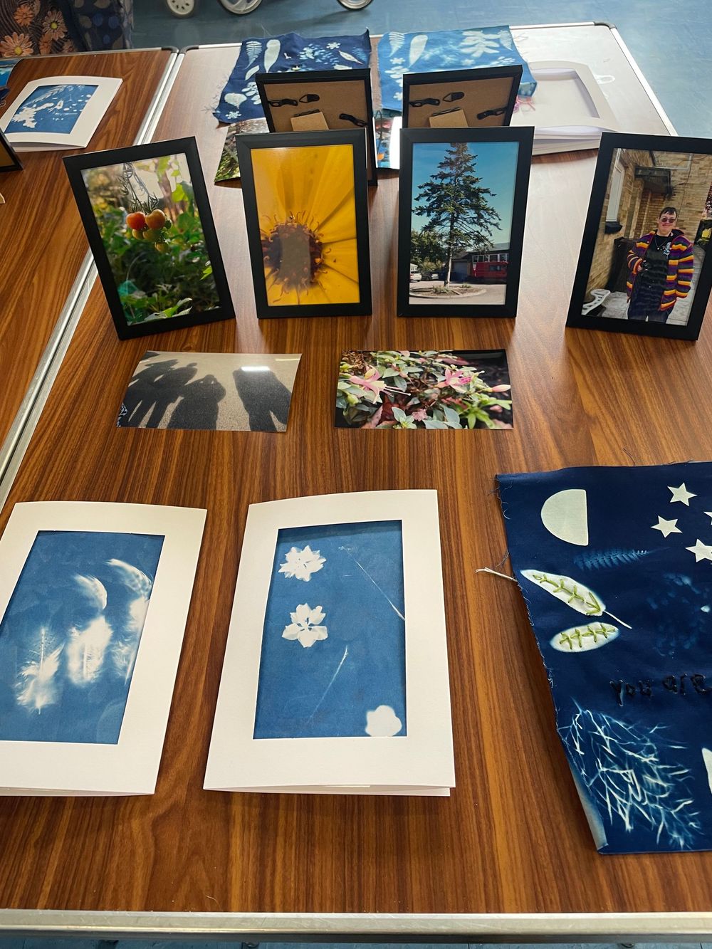 A series of framed artwork and photographs displayed on a wooden table showing nature scenes and abstract designs.