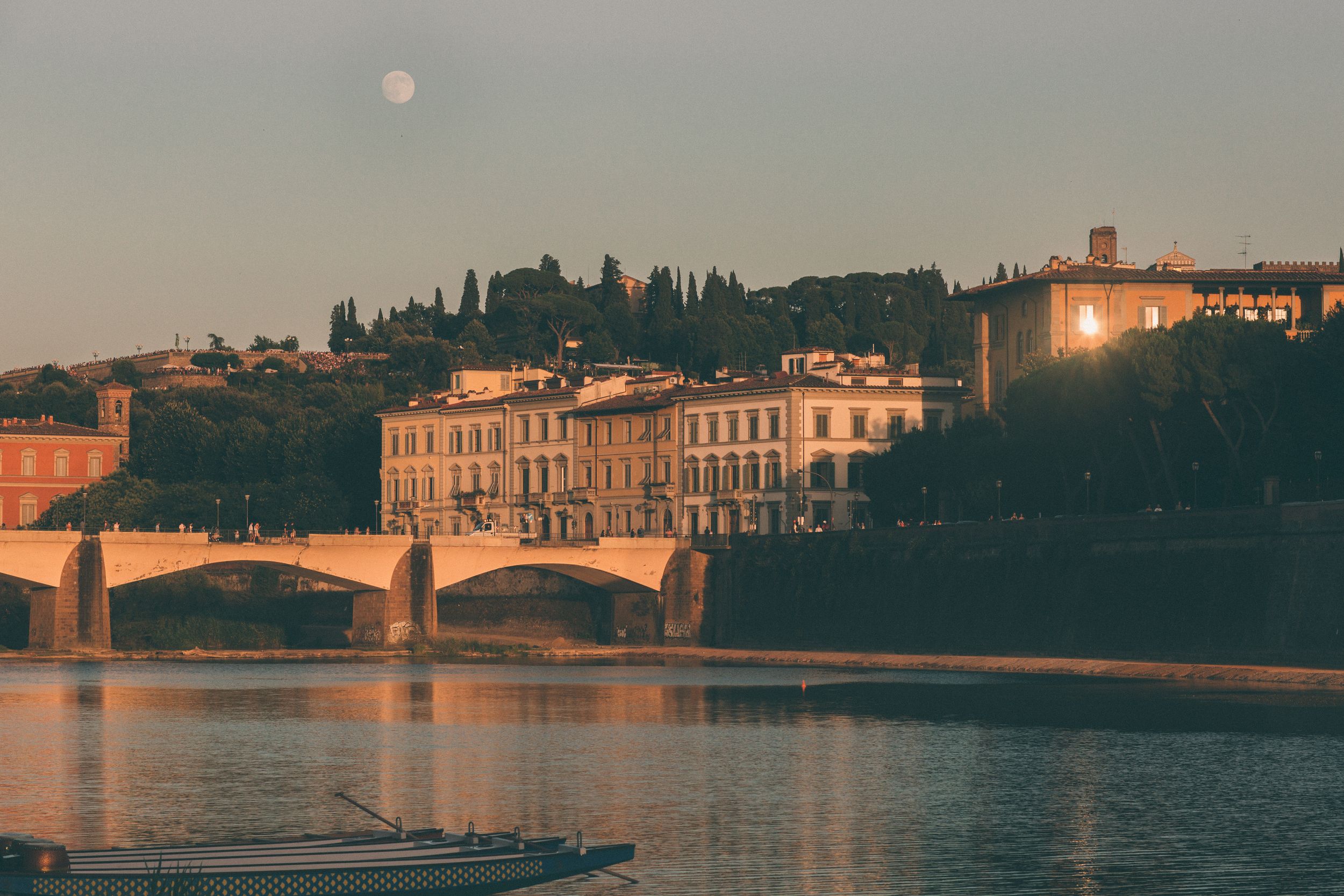 Historic buildings line the waterfront of Florence, Italy at sunset as golden light reflects off the Arno River.