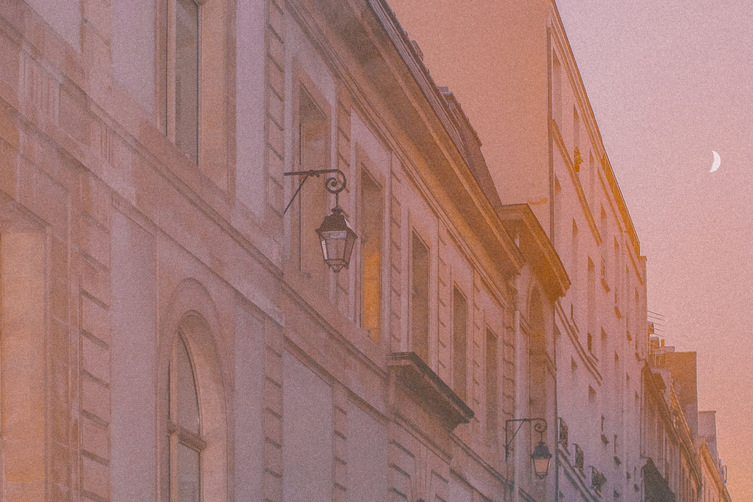 Historic European street with ornate stone buildings and lanterns at dusk creating a warm, romantic atmosphere.