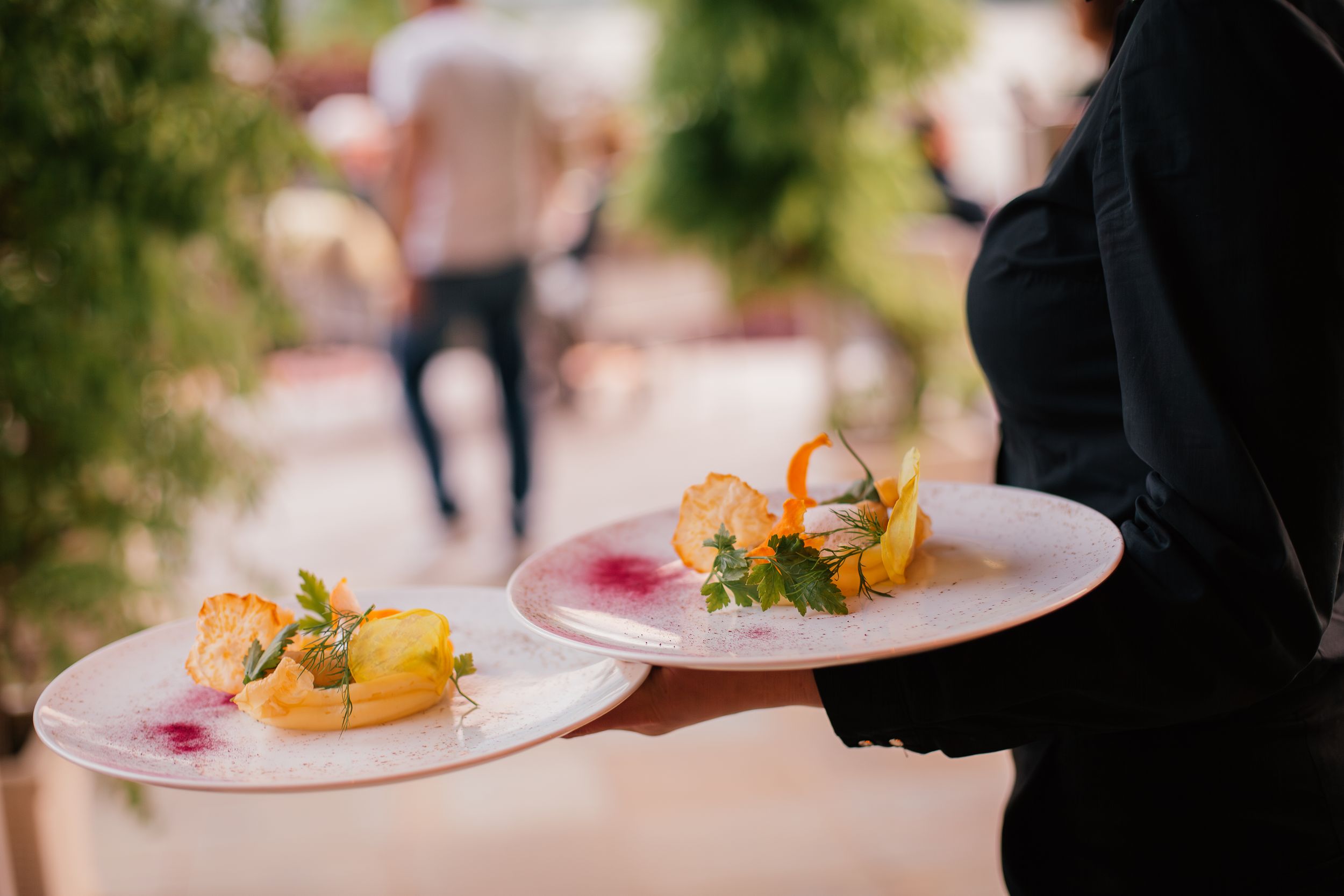 Elegant plated desserts with colorful garnishes and edible flowers served at an outdoor dining event.