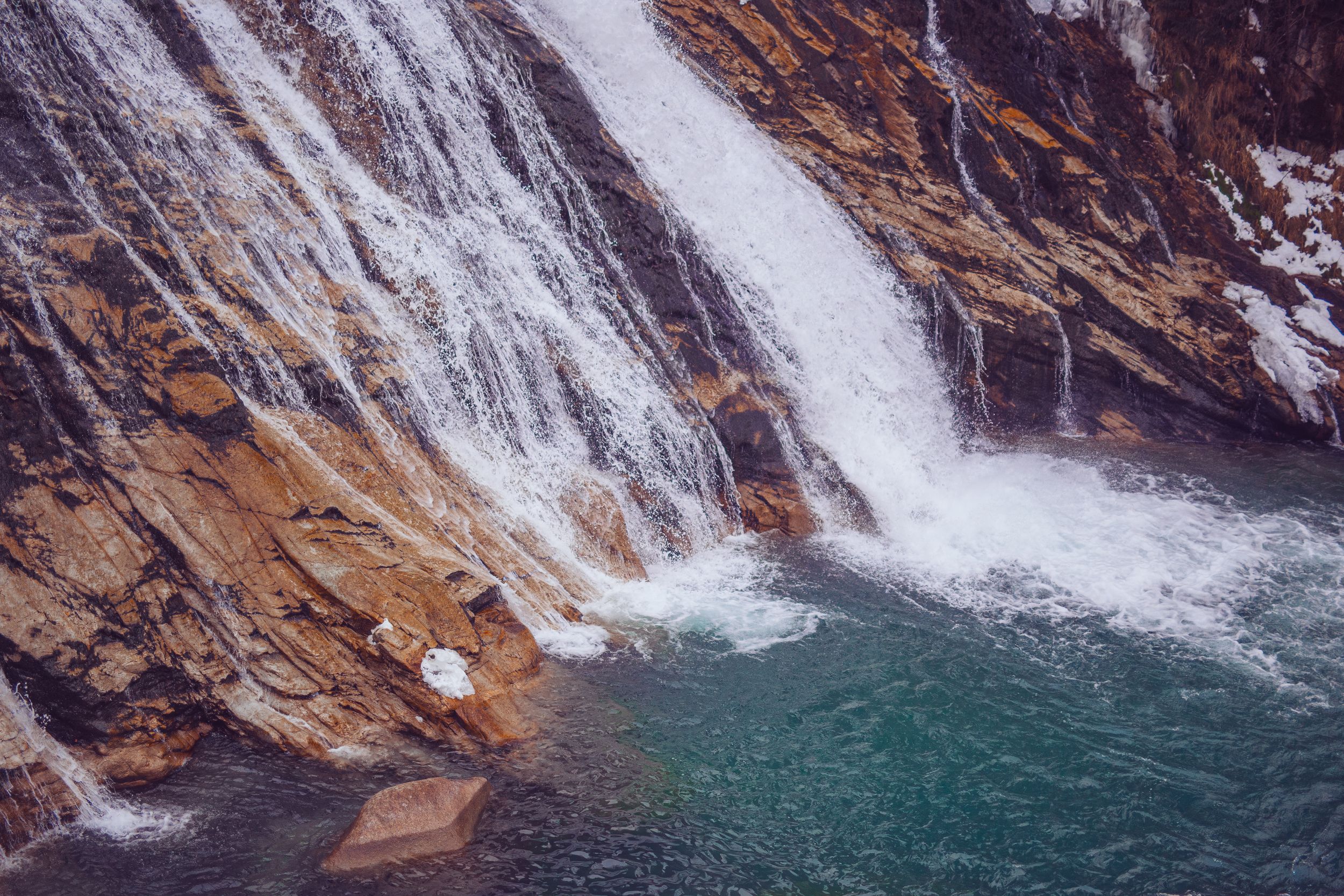 Scenic waterfall cascades down rocky cliffs into turquoise pool surrounded by rugged mountain terrain.