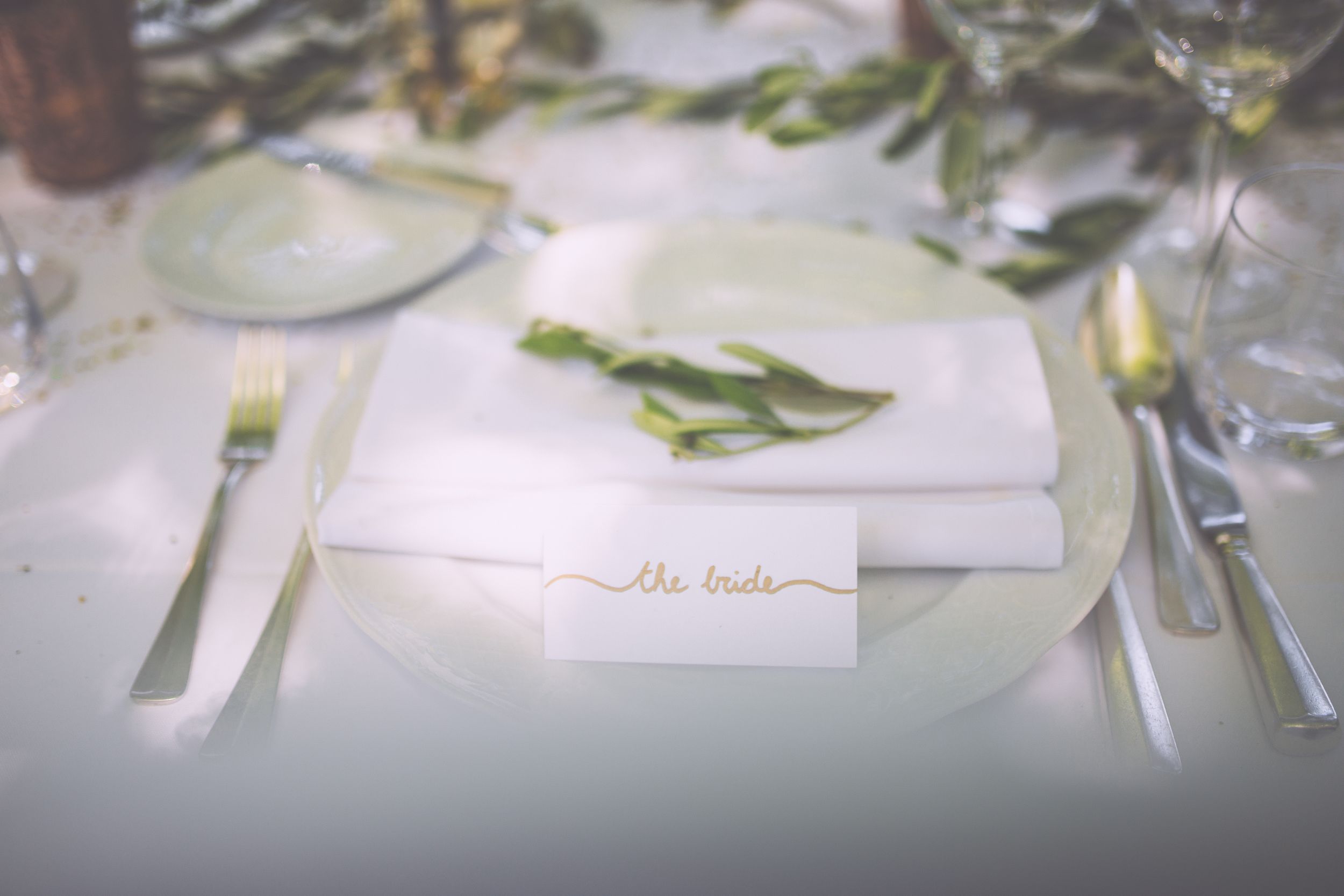 Wedding place cards with greenery decorations and calligraphy sit elegantly on a white tablecloth.