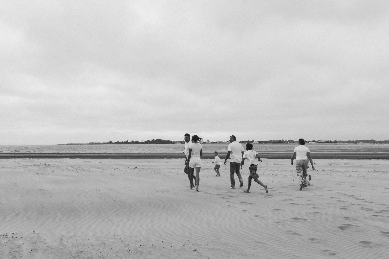 Family running together on the beach at West Wittering, smiling and enjoying the moment.