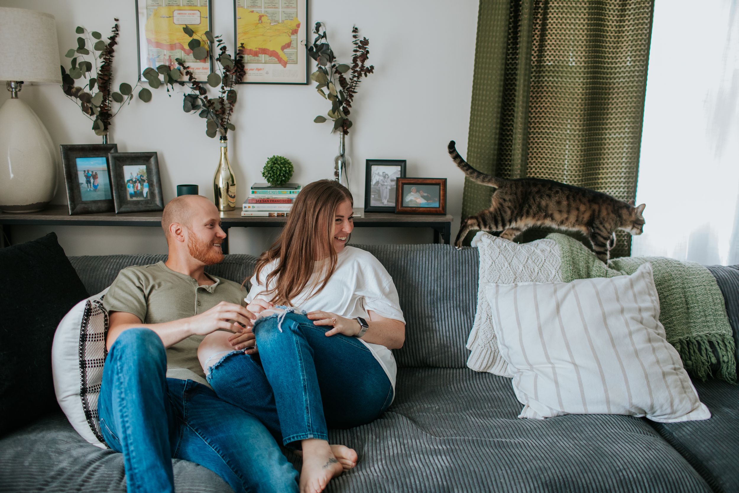 Couple in blue denim sitting together on a gray couch in a cozy living room with plants and natural light.
