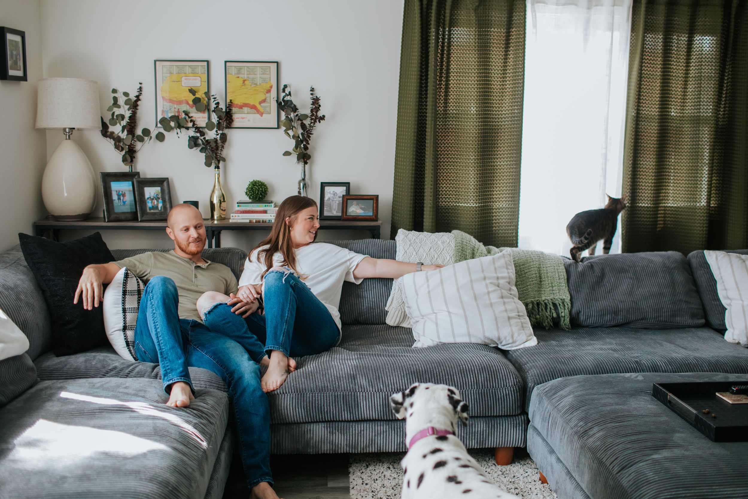 Family relaxes together on a gray couch in a cozy living room with natural lighting.