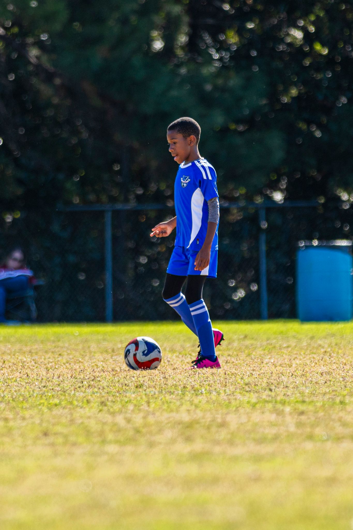 Young soccer player in blue jersey practicing ball control drills on sunny grass field.