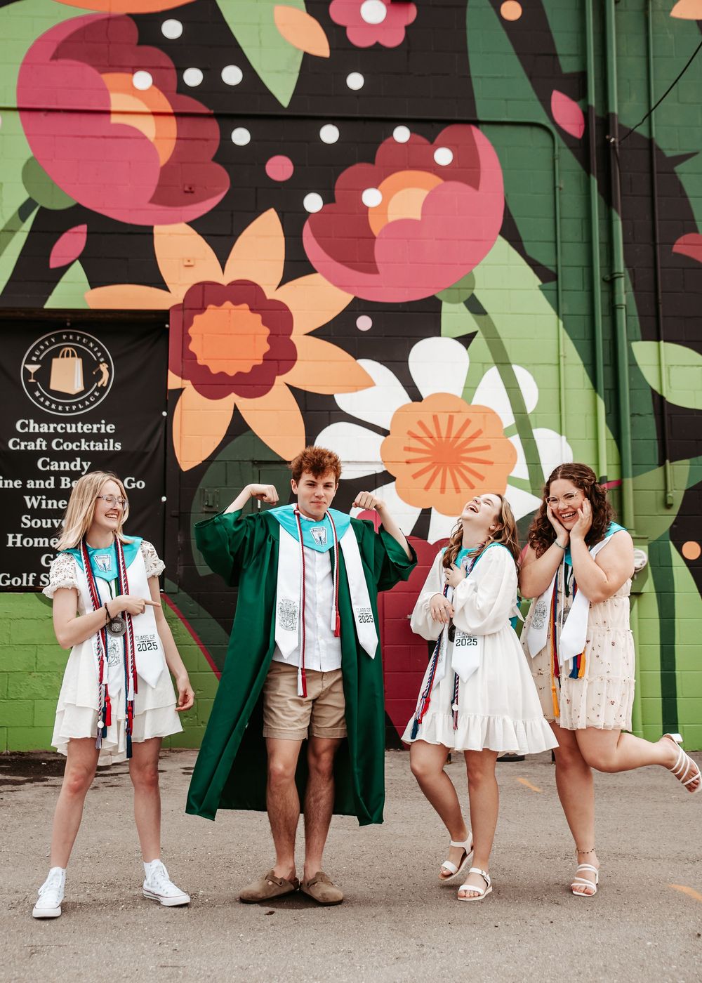 A group stands against a colorful floral mural wall wearing white outfits with green jackets.