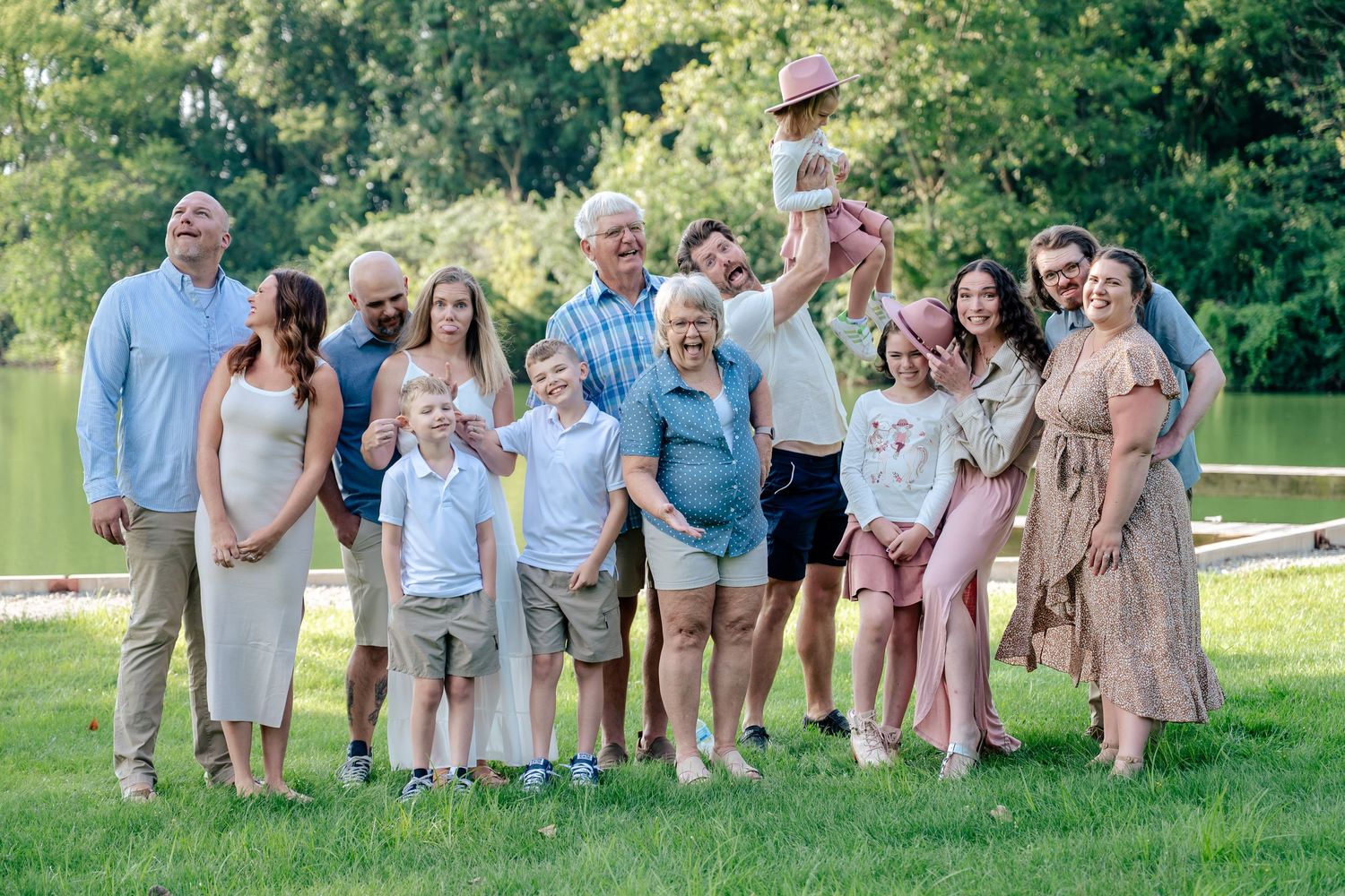 Large group wearing coordinated neutral-toned outfits poses together on grassy lawn during summer outdoor photo session.