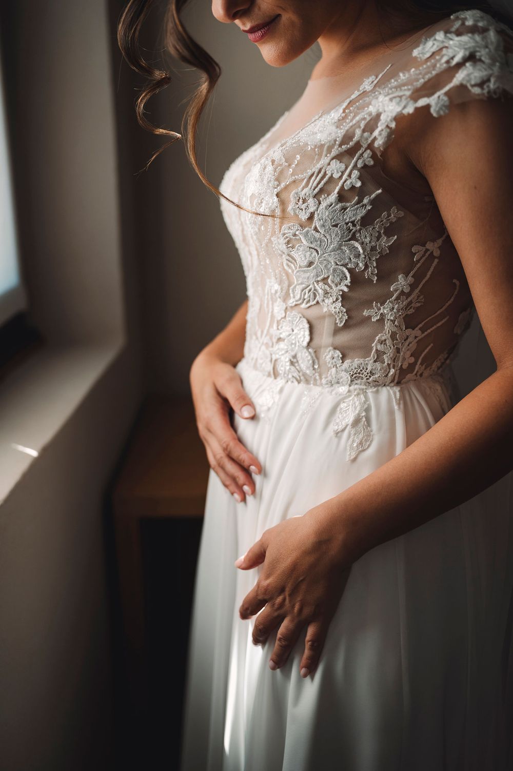 Dettagli ravvicinati del delicato pizzo bianco e delle perline sul corpetto di un abito da sposa con gonna fluida in chiffon.