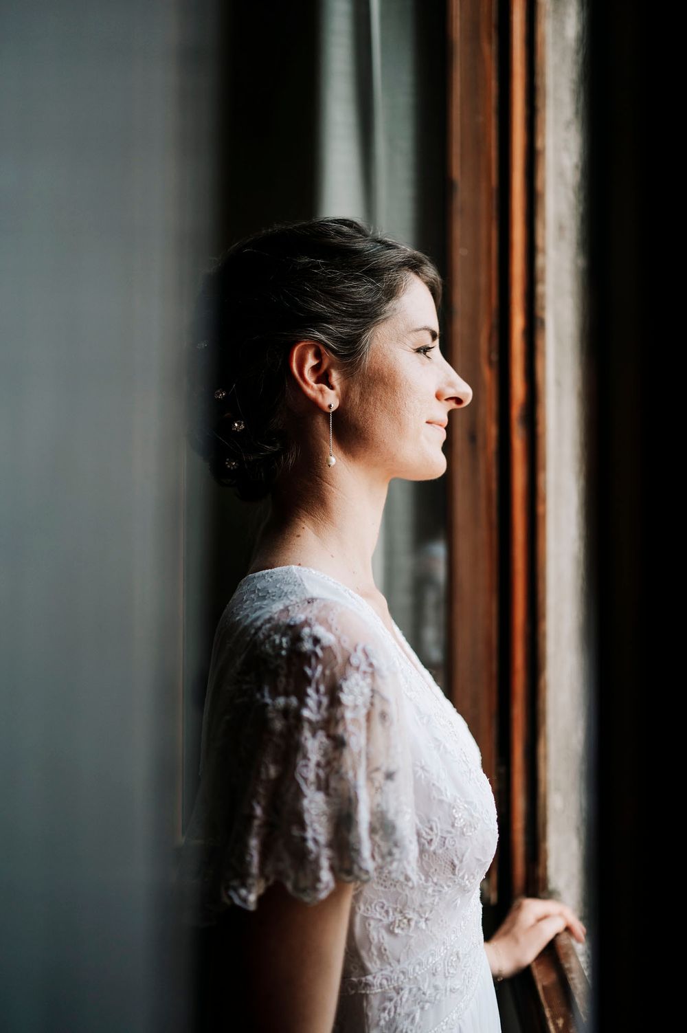 Donna in abito di pizzo bianco guarda fuori dalla finestra in un'elegante serie di ritratti di profilo.