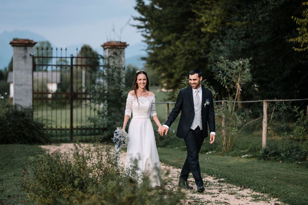 Sposi che camminano insieme lungo un sentiero immerso in un rigoglioso giardino con pilastri in pietra.