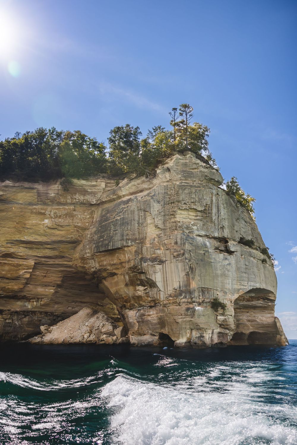 Rugged limestone cliffs rise from turquoise waters under clear blue skies at Pictured Rocks National Lakeshore.
