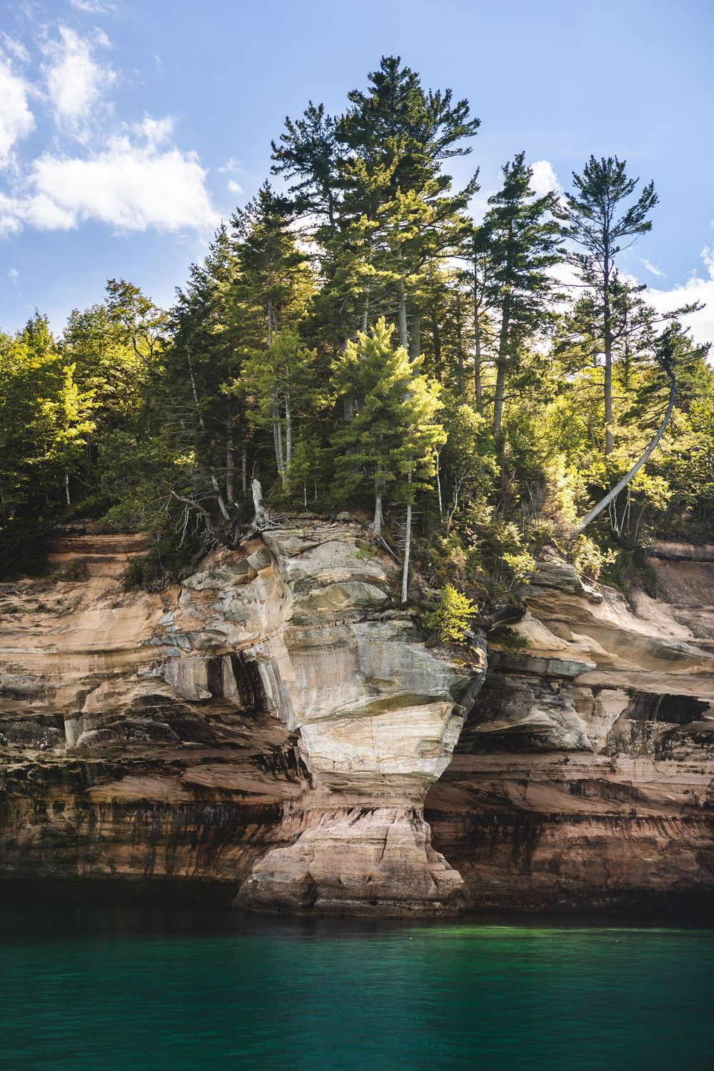 Towering sandstone cliffs with evergreen trees rise above the emerald waters of Lake Superior at Pictured Rocks.