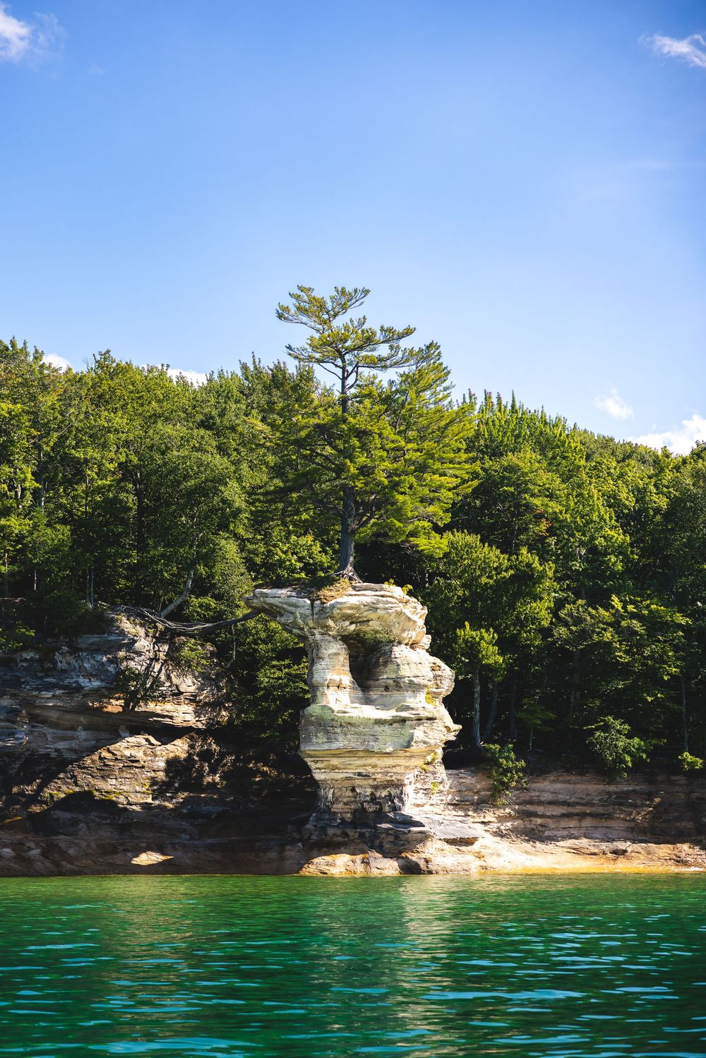 Emerald waters lap against eroded sandstone cliffs surrounded by lush forest at Pictured Rocks National Lakeshore.