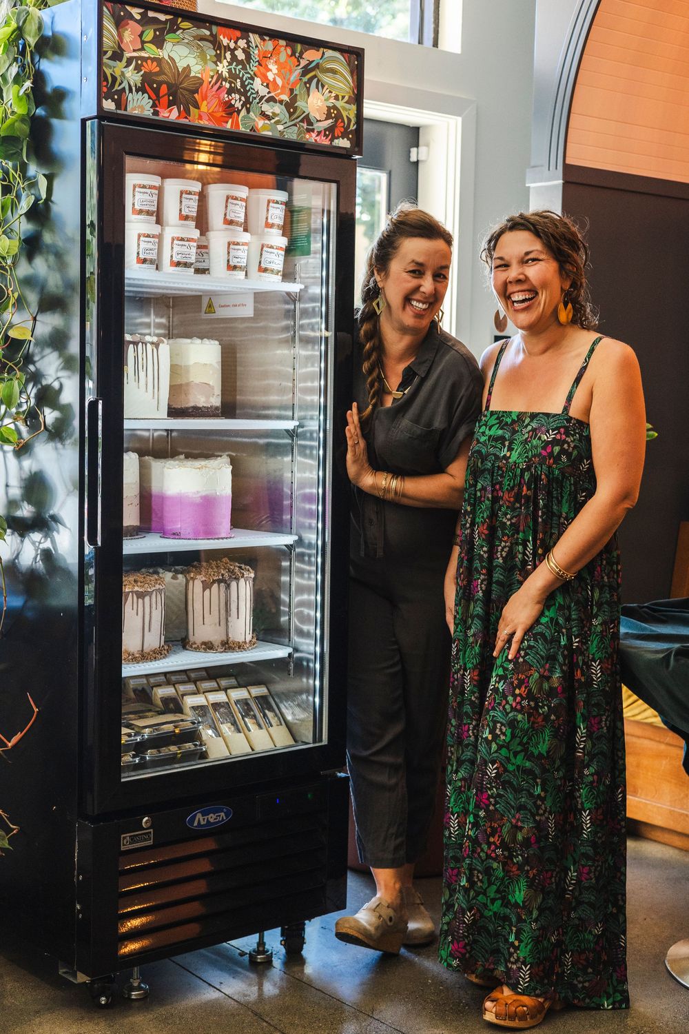 Two people in casual attire share a joyful moment while standing next to a commercial refrigerator display case.
