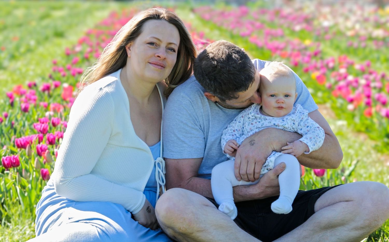 Family relaxing together in blooming tulip field during springtime photo session.