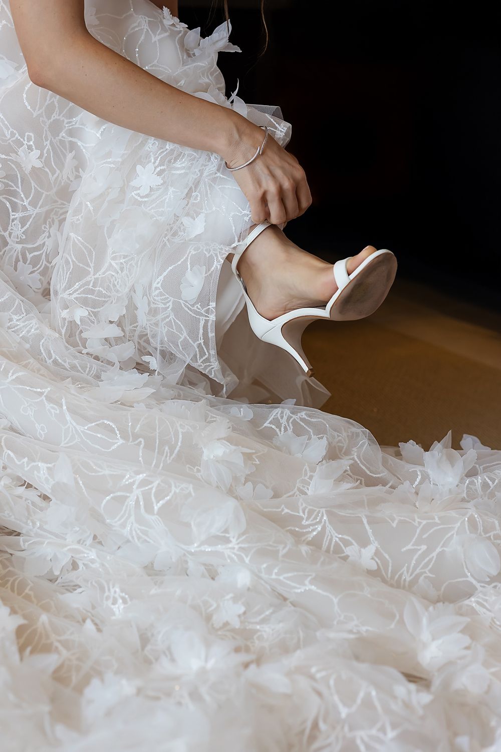 A close-up view of elegant white bridal shoes peeking out from beneath layers of delicate tulle fabric.