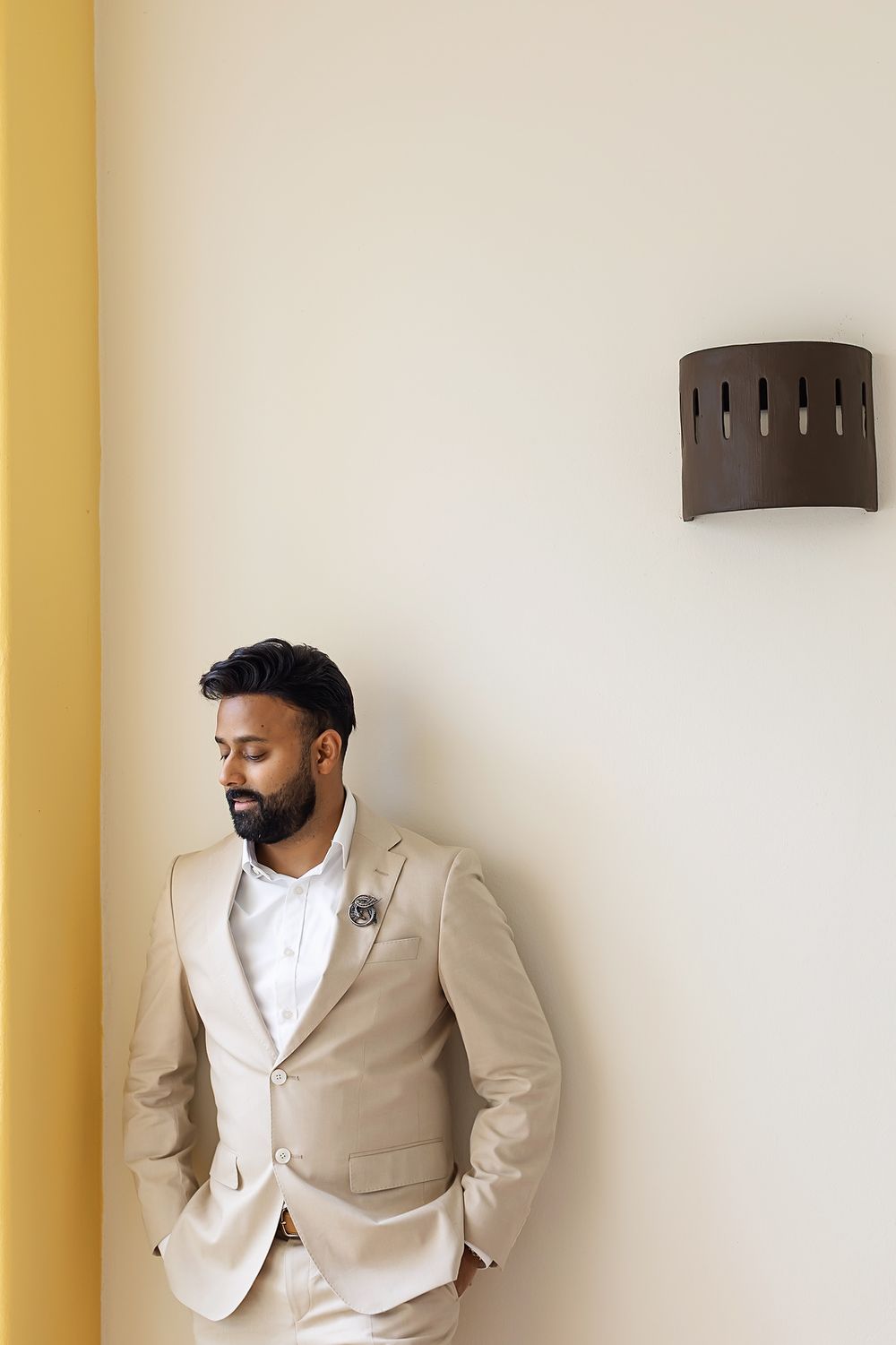 A groom poses in a stylish beige suit and white shirt against a neutral wall in multiple portrait angles.