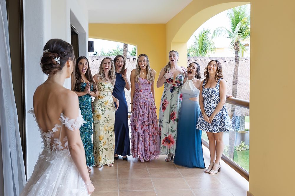 Wedding party members in colorful floral dresses gather in a sunlit hallway at a tropical venue.