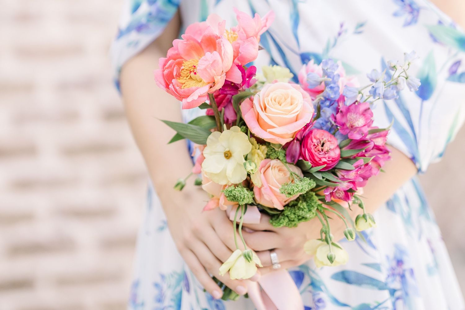 A vibrant bouquet of pink roses and mixed flowers held in hands wearing a floral dress.