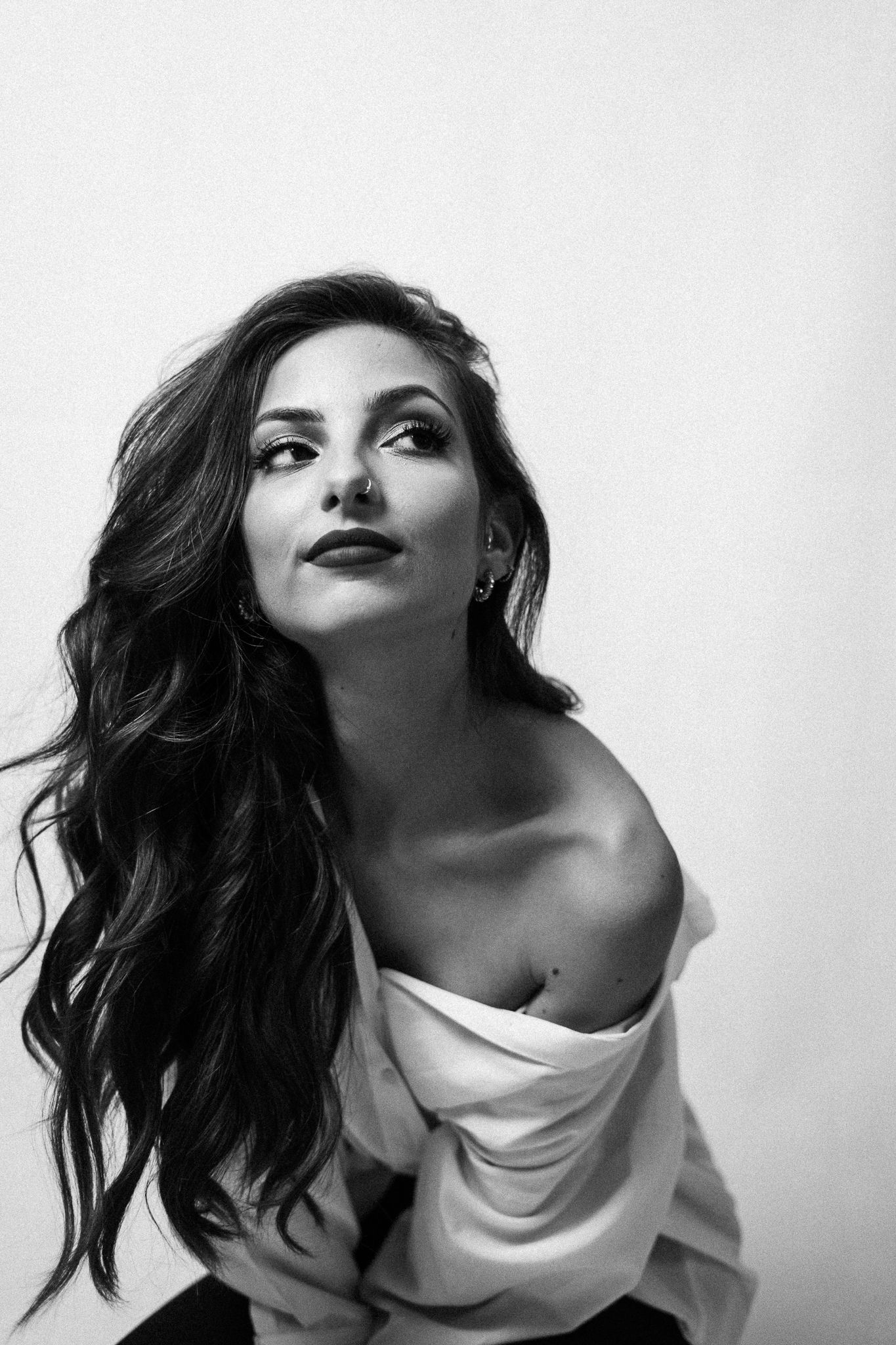 Dramatic black and white portrait with elegant off-shoulder pose against white background.